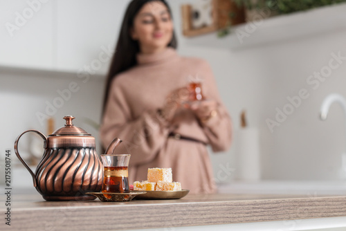 Turkish tea with delight on table against woman in kitchen, closeup