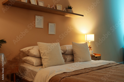 Interior of dark room with bed and glowing lamp at night