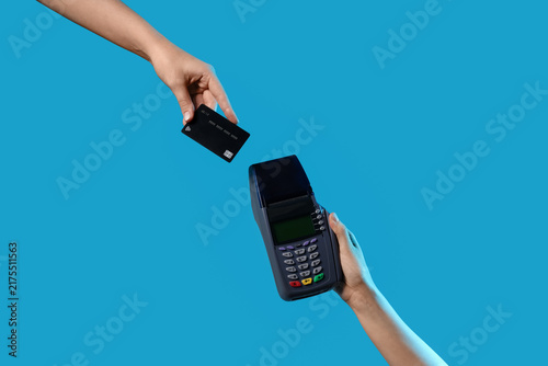 Hands holding payment terminal with credit card on blue background