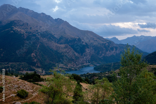 Obraz na płótnie A view down a Pyrenees valley to the reservoir far below with rugged peaks under evening clouds near Formigal Spain a moody and majestic mountain landscape of the Tena Valley