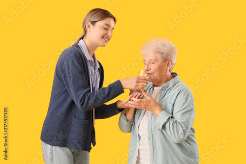 Senior woman with nurse drinking water on yellow background