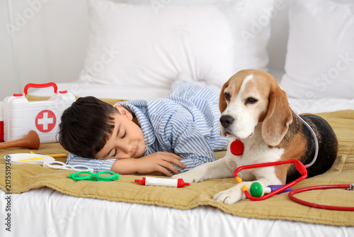 Cute little doctor with Beagle dog and toys sleeping in bedroom