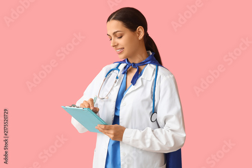 Beautiful female doctor in superhero costume with clipboard on pink background