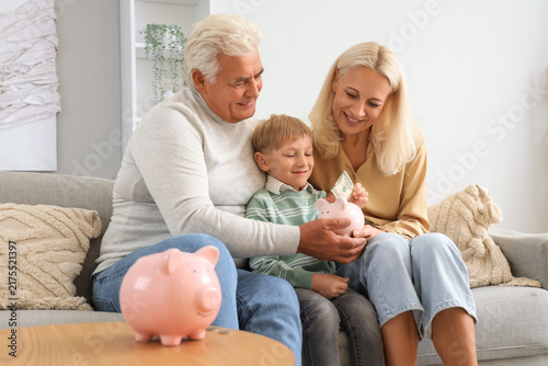 Fotografía Little boy with his grandparents putting money in piggy bank at home