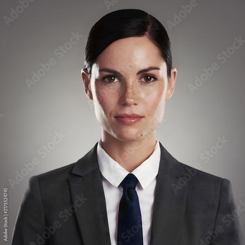 Professional portrait of a confident businesswoman in a formal suit and tie, photographed against a neutral background with studio lighting, suitable for corporate and business concepts.