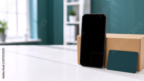 Smartphone with a credit card and cardboard box on a white table. Mobile shopping and online payment concept. Digital banking and e-commerce mockup