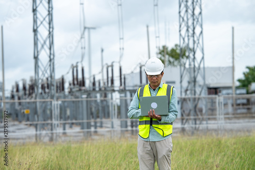 Engineer workout at electrical substation using laptop outdoors, wearing safety equipment and concentrating on field inspection work