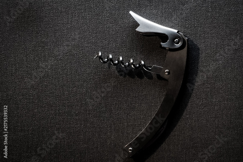 Cuadro en lienzo Close-up shot of a classic stainless steel waiter's corkscrew and bottle opener resting on a textured black background with dramatic lighting and soft shadows