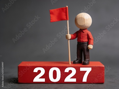 Miniature Figure Holding Red Flag on 2027 Block Symbolizing New Year Goals and Achievement


