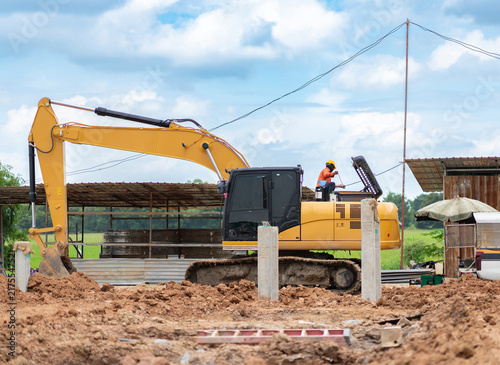 Canvastavla Yellow excavator machine parked at a construction site with a worker performing engine maintenance under a blue sky