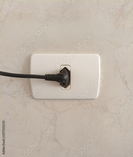 Black electrical plug connected to a white wall socket on a tiled wall
