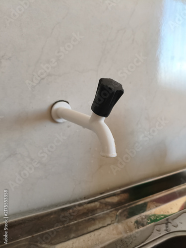 White plastic water faucet with a black handle on a light wall
