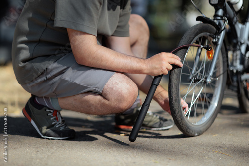   Man Inflating Bicycle Tire With Portable Mini Pump Outdoors. Person crouches down to pump up the front wheel of his bicycle