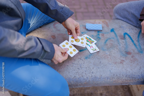 People playing scopa card game outdoors on bench