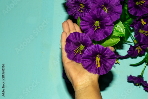 Foto Open palm supporting violet artificial flowers on blue background