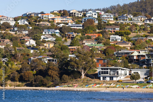 Houses densely scattered over a coastal hill with beach and water in the foreground at Blackmans Bay