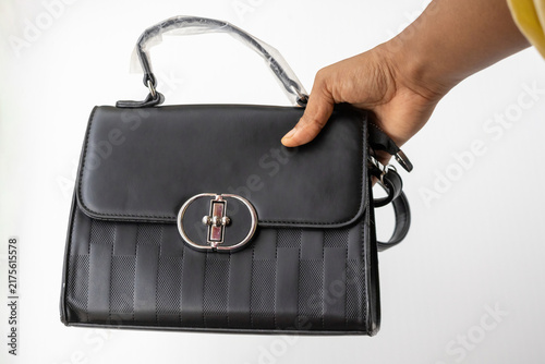 Foto Human hand holding black leather handbag with silver lock over white background