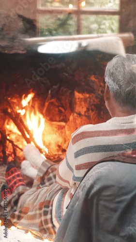 Unrecognizable couple snuggling under a warm plaid blanket while relaxing in front of a crackling fireplace, creating a cozy and romantic atmosphere for a perfect winter evening at home