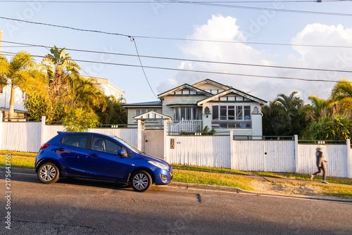 old gabled bungalow in a suburban street at sunset with a blue car parked on the street in front