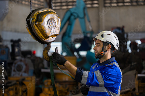 Caucasian engineer worker is using overhead crane hoist to carry raw materials inside metal sheet manufacturing factory for heavy industry