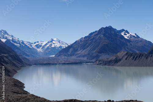 Konstfotografi Tasman Glacier and glacial lake surrounded by rugged snow-capped mountains in Aoraki Mount Cook National Park, South Island, New Zealand, beneath a clear blue sky