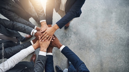 High-angle view of diverse corporate professionals joining hands in a modern conference room setting to symbolize unity, teamwork, and success