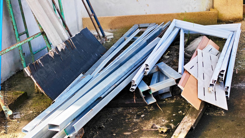Scrap Metal Pile: Stacked aluminum window, door frames and steel profiles stored, lies discarded on the ground, suggesting construction waste or recycling at home renovation area.