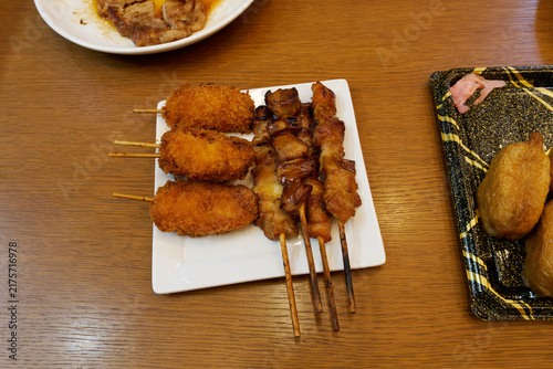 Obraz na plátně Assorted Japanese skewers including deep-fried kushikatsu and grilled yakitori served on a white square plate on a wooden table
