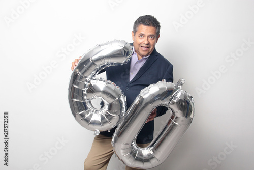 60-year-old Latino man with a dark skin displays 60 shaped balloons to celebrate his birthday and his entry into his old age
