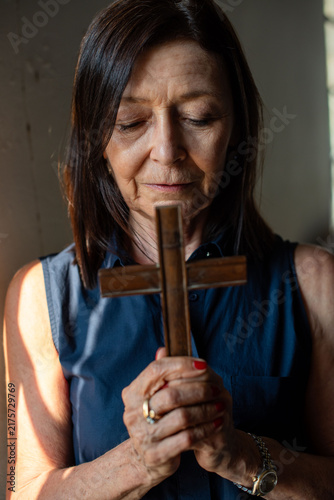 Fotografie Middle-aged white woman praying with wooden cross, eyes closed