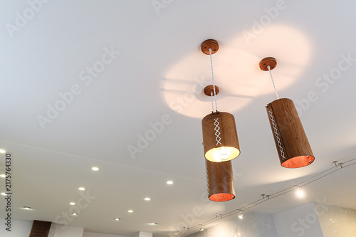 Foto Wooden cylindrical pendant lights with white stitching details hang from ceiling, casting warm circular glows
