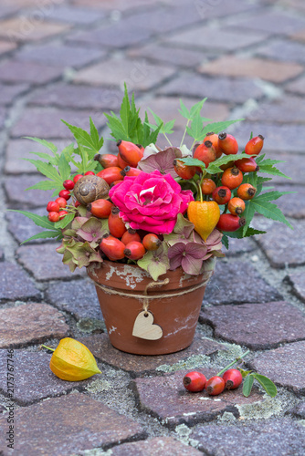 florales Arrangement mit roter Rose, Hagebutten, Hortensienblüten, Physalis und Ahornblättern im Terracotta-Topf