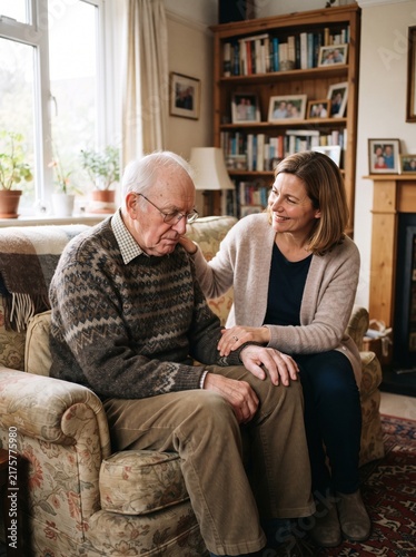 Caregiver comforting sad elderly man sitting in armchair at home