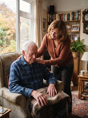 Caregiver comforting elderly man sitting in armchair at home