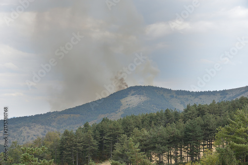 Forest fire on the mountain top. Thick smoke can be seen in the distance.