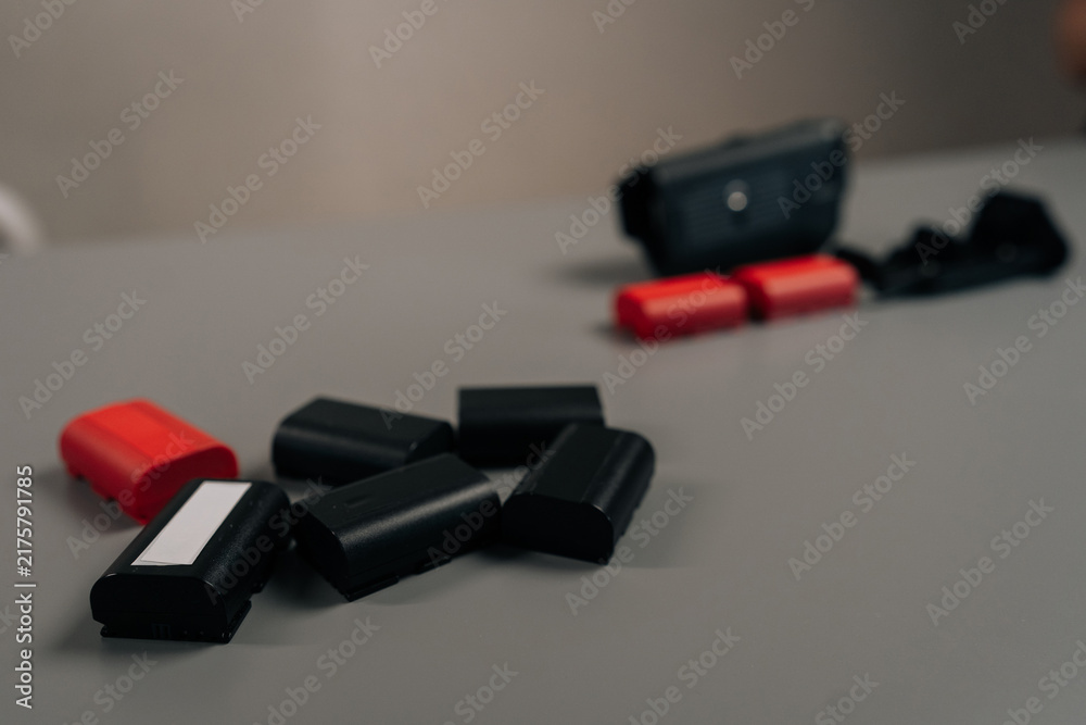 Naklejka premium Camera digital system with power supply accessory and multiple charged, discharged red and black lithium-ion rechargeable battery packs for professional photography equipment, close-up, cropped shot.