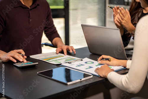 Business team reviewing financial charts and using calculator, laptop and tablet during a meeting at an office table.