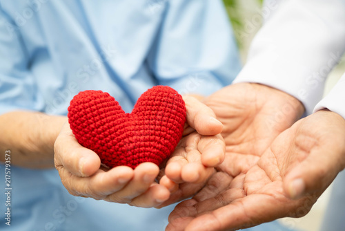 Asian woman doctor holding red heart with senior patient for health in hospital.