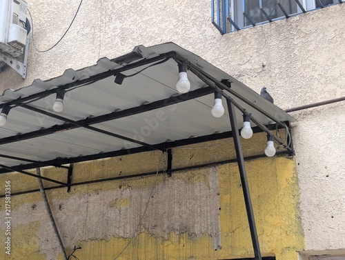 A grimy polycarbonate awning over an entryway, dotted with dusty, unlit lamps. The cracked cover and rusted fixtures show its age in broad daylight.

