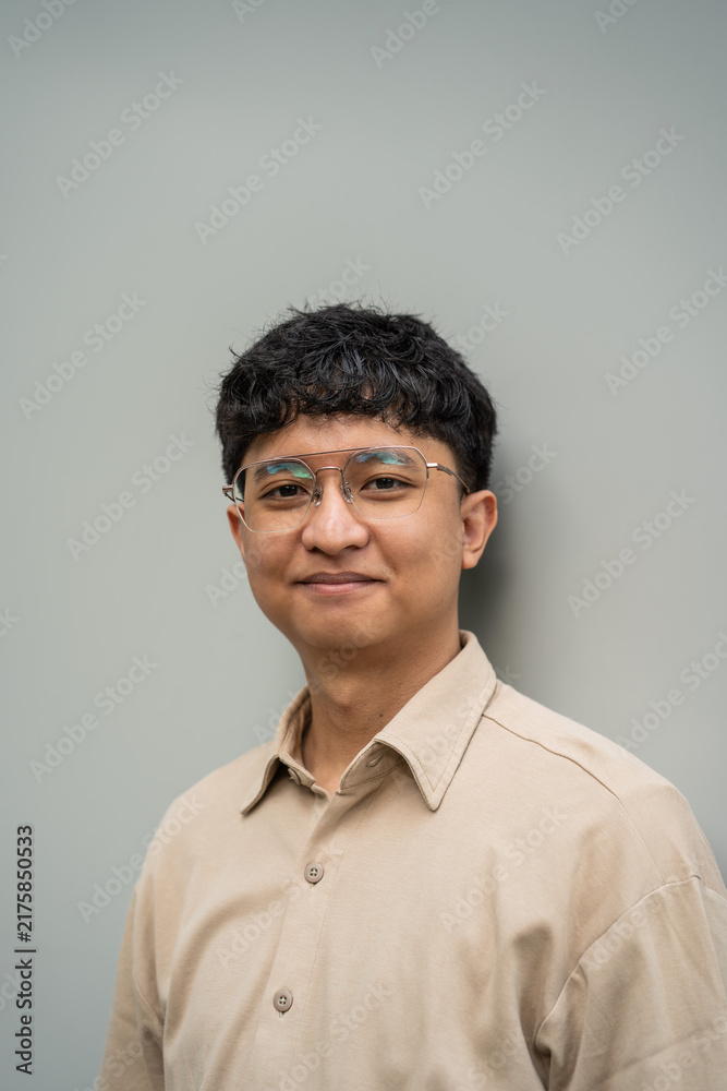 Obraz premium A smiling man with glasses poses for a portrait against a light gray background.