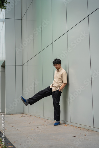 Obraz na plátne A young man casually leans against a modern gray wall while lifting one foot