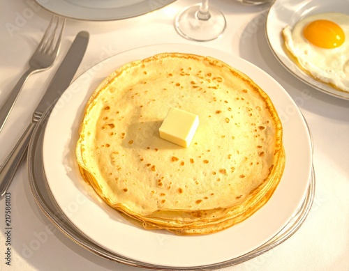 Stack of golden crepes on a white plate and silver charger, ready for a delicious breakfast