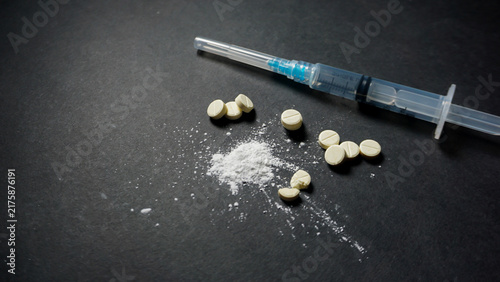 фотографія Some white illegal drugs in powder and pill form with one sealed disposable syringe