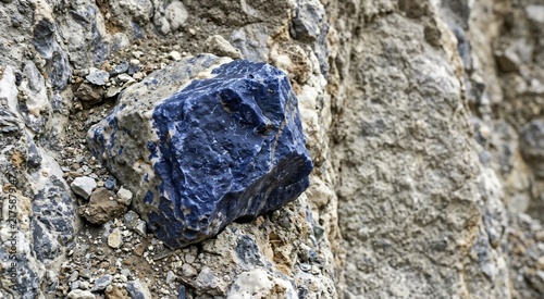 Rough blue sodalite stone embedded in natural rocky surface. Raw unpolished mineral specimen in geological environment