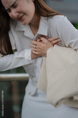 Obraz na plátně Chest pain concept of a young businesswoman clutching her chest with sudden discomfort while at work, showing a painful health problem