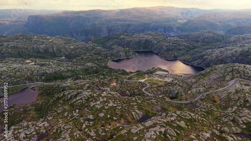 Aerial view of a mountain lake and the winding Lysevegen road crossing the rugged rocky plateau above Lysebotn in Rogaland, Norway.
