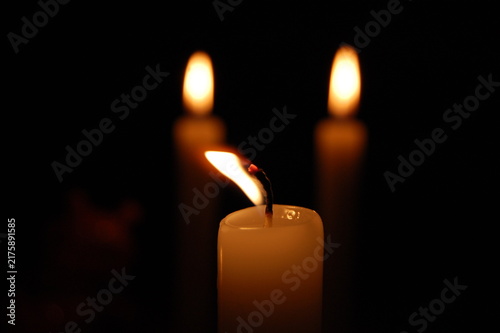 Fotografie Close-up of a burning candle with a bright glowing flame reflected in a dark surface, isolated against a black background