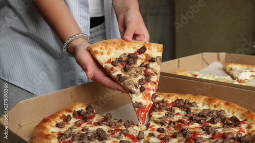 Hands hold a delicious slice of pizza with meat, mushrooms, and cheese, pulled from a cardboard box. The atmosphere is cozy, like a beef pizza lunch or dinner.