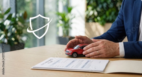 Businessman protecting a red model car above an auto insurance policy on a wooden desk. Vehicle insurance, financial protection and risk management concept with copy space.