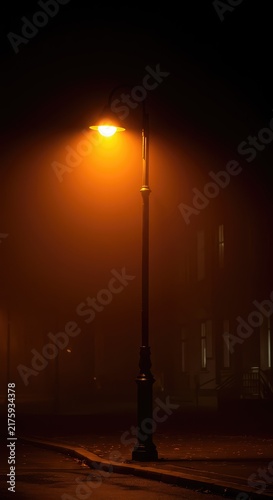 A vibrant amber glow emanating from a classic street lamp fixture illuminates the dark and misty atmosphere on a lonely evening ,misty ,amber ,exterior
